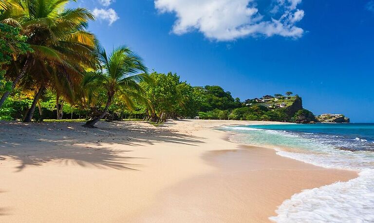 A scenic view of Grenada’s coastline with white sand, turquoise water, and lush greenery, representing the natural beauty and peaceful atmosphere of the Spice Island.